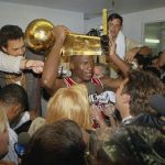 
              FILE - Chicago Bulls Michael Jordan holds the NBA Championship trophy aloft while talking with the media in the locker room after their 108-101 win against the Los Angeles Lakers at Inglewood, Calif., June 13, 1991. (AP Photo/Reed Saxon, File)
            