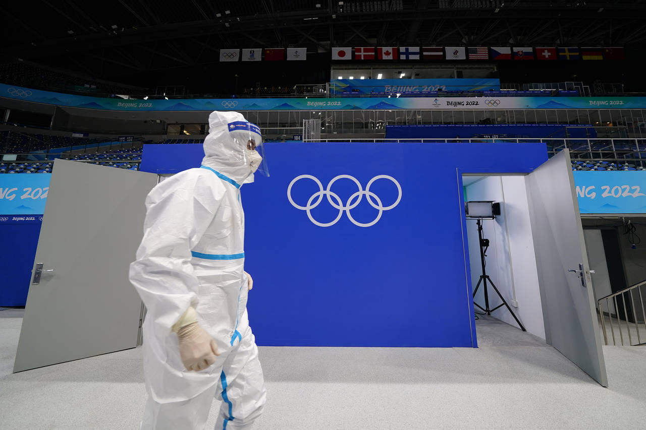 FILE - A worker in protective gear walks past the Olympic rings at the National Indoor Stadium at t...