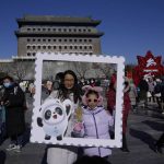 
              Residents pose for photos with a cutout showing the Olympic mascot Bing Dwen Dwen at a popular retail street in Beijing, China, Friday, Feb. 4, 2022. (AP Photo/Ng Han Guan)
            