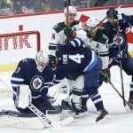 
              Winnipeg Jets goaltender Connor Hellebuyck (37) saves the puck despite players crashing into him during the second period of the team's NHL hockey game against the Minnesota Wild on Wednesday, Feb. 16, 2022, in Winnipeg, Manitoba. (John Woods/The Canadian Press via AP)
            