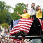
              FILE - Olympian Sunisa Lee, center, waves from a St. Paul fire truck with her mom Yeev Thoj, left, and sister Shyenne Lee as fans cheer for her along the parade route, Aug. 8, 2021, in St. Paul, Minn. (Jerry Holt/Star Tribune via AP, File)
            