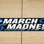 
              FILE -The March Madness logo is shown on the court during the first half of a men's college basketball game in the first round of the NCAA tournament at Bankers Life Fieldhouse in Indianapolis, Saturday, March 20, 2021. Kansas, Villanova, North Carolina and Duke will play in the first Final Four to take place under the new world of “name, image and likeness” endorsements in college sports. It allows college players to earn money through endorsements. (AP Photo/Paul Sancya, File)
            