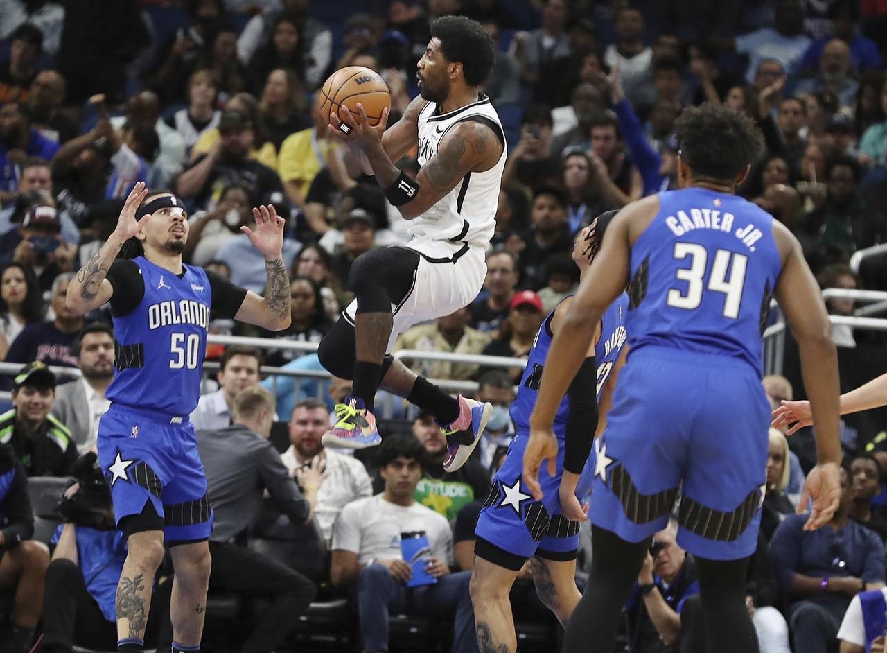 Brooklyn guard Kyrie Irving, center, leaps to shoot among Orlando defenders during an NBA basketbal...