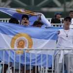 
              Young men hold Argentine flags, some modified with the logo of the Ultra Music Festival, as they cheer for Francisco Cerundolo of Argentina after he won his quarterfinal match when opponent Jannik Sinner of Italy retired during the first set, at the Miami Open tennis tournament, Wednesday, March 30, 2022, in Miami Gardens, Fla. (AP Photo/Rebecca Blackwell)
            
