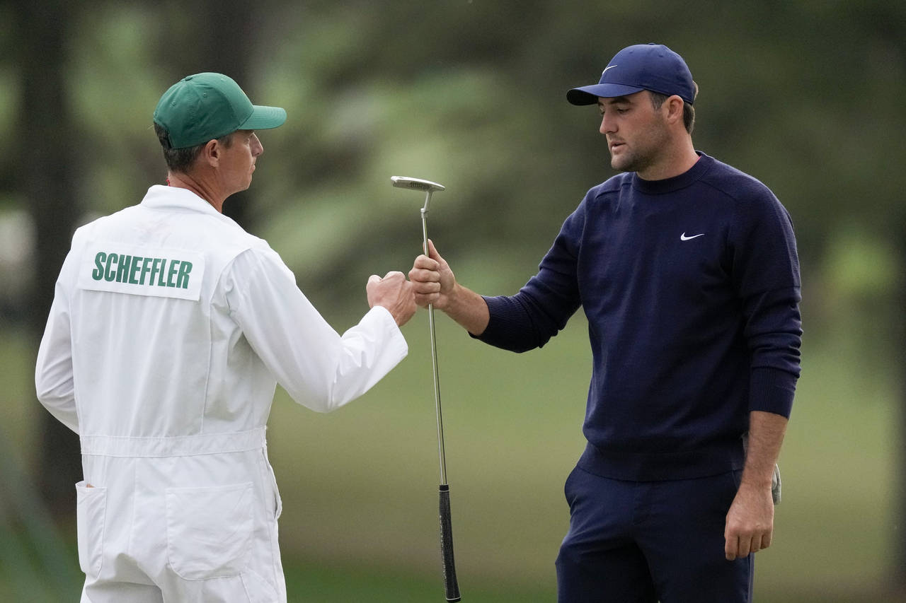 Scottie Scheffler bumps fists with his caddie, Ted Scott, after putting in on the 18th green during...