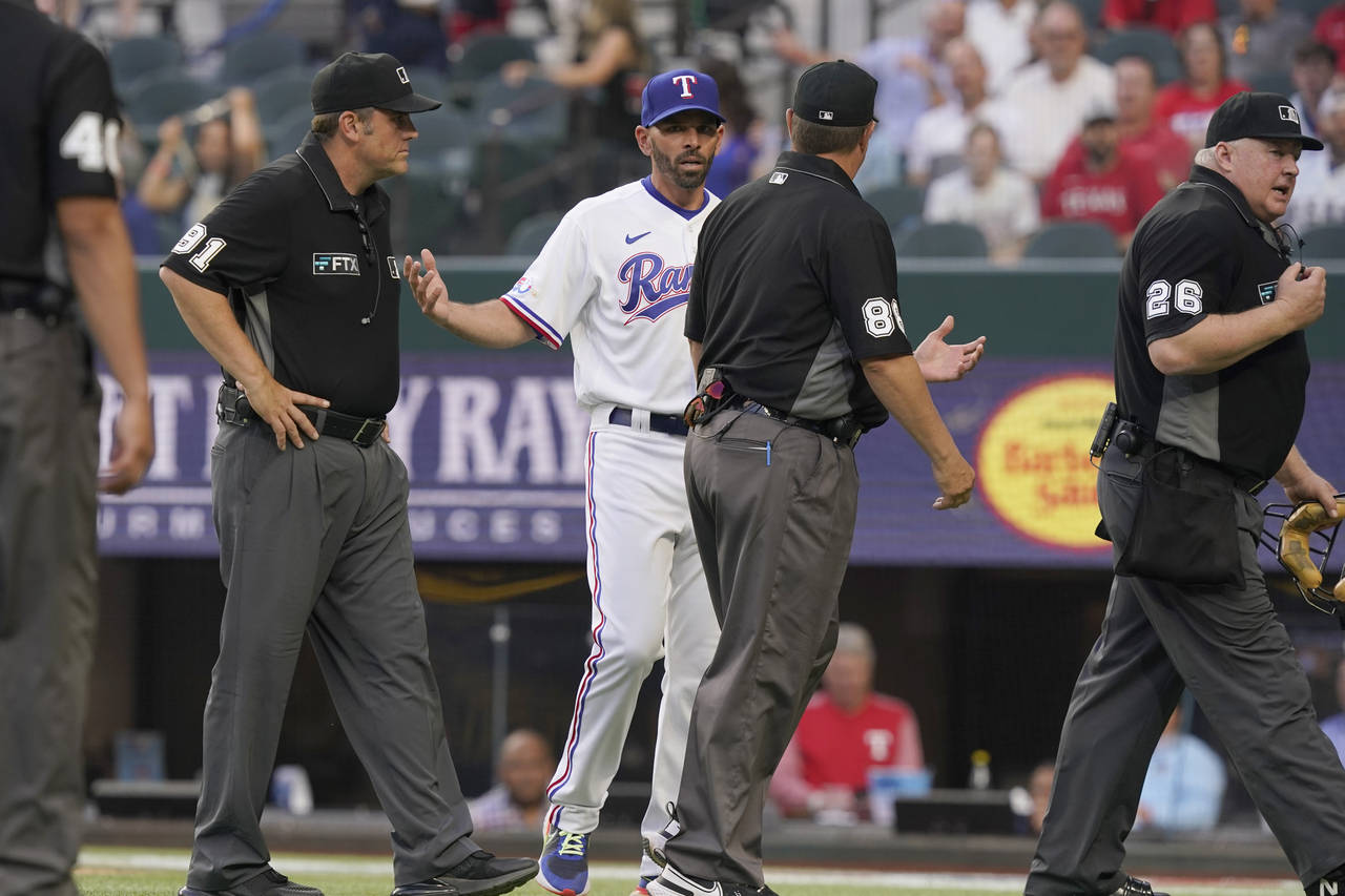 Texas Rangers manager Chris Woodward, center left, questions a call as the umpire crew walks off th...