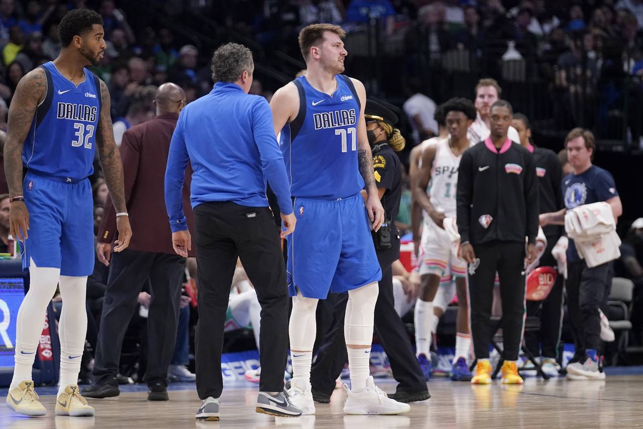 Dallas Mavericks' Marquese Chriss and a member of the staff check on guard Luka Doncic (77) who suf...