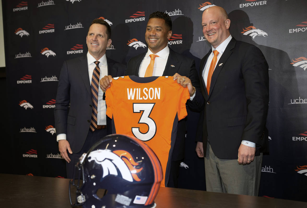 FILE - Denver Broncos new starting quarterback Russell Wilson, center, is flanked by coach Nathanie...