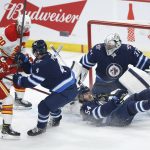 
              As Winnipeg Jets' Dylan Samberg (54) goes down goaltender Connor Hellebuyck (37) saves the shot from Calgary Flames' Dillon Dube (29) as Jets' Neal Pionk (4) defends during the first period of an NHL hockey game, Friday, April 29, 2022 in Winnipeg, Manitoba. (John Woods/The Canadian Press via AP)
            