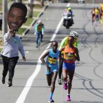 
              A man carrying a picture of actor Will Smith runs behind Peres Jepchirchir, of Kenya, left, and Ababel Yeshaneh, of Ethiopia, during the 126th Boston Marathon in Natick, Mass, Monday, April 18, 2022. (AP Photo/Jennifer McDermott)
            