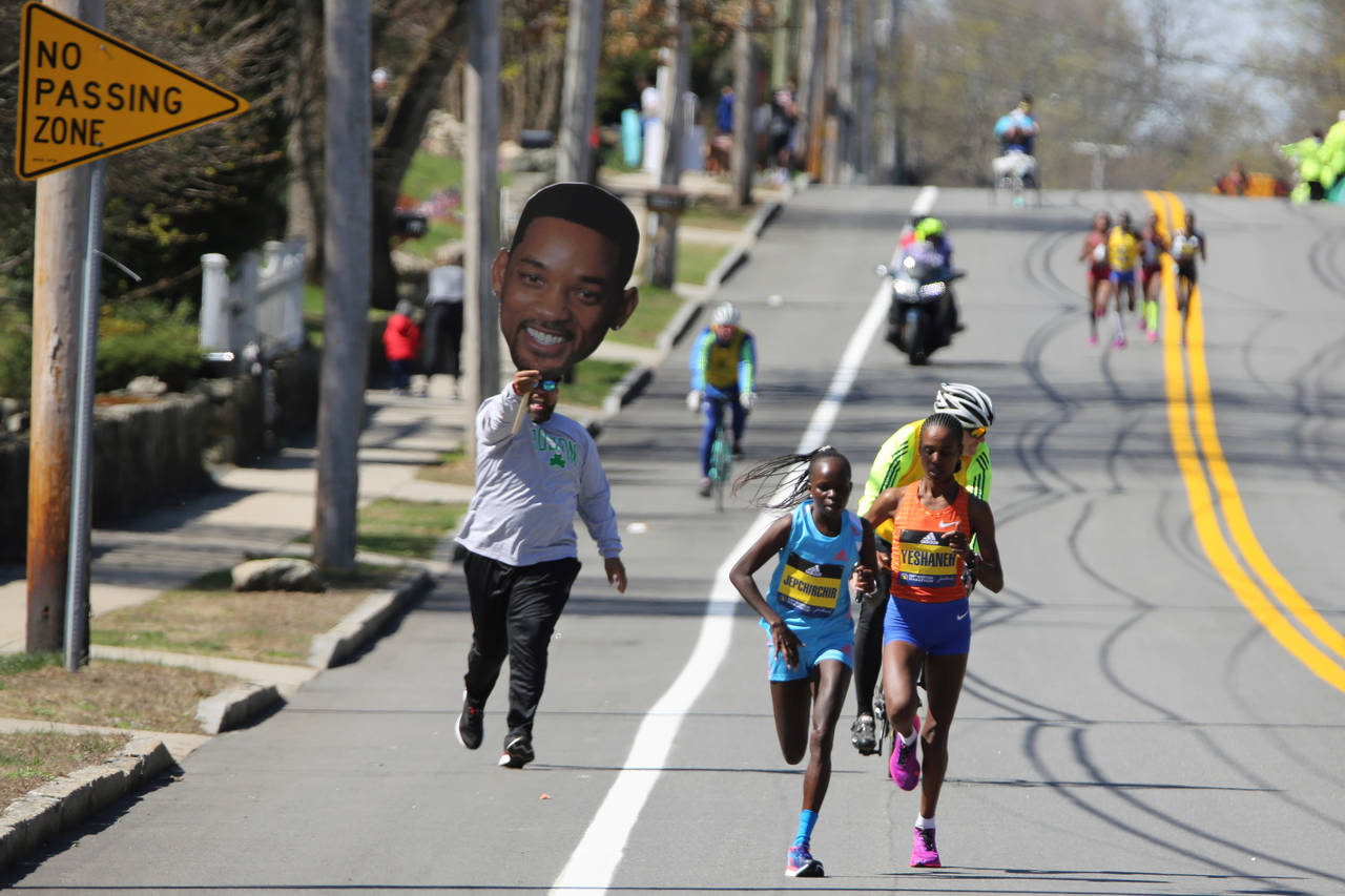 A man carrying a picture of actor Will Smith runs behind Peres Jepchirchir, of Kenya, left, and Aba...
