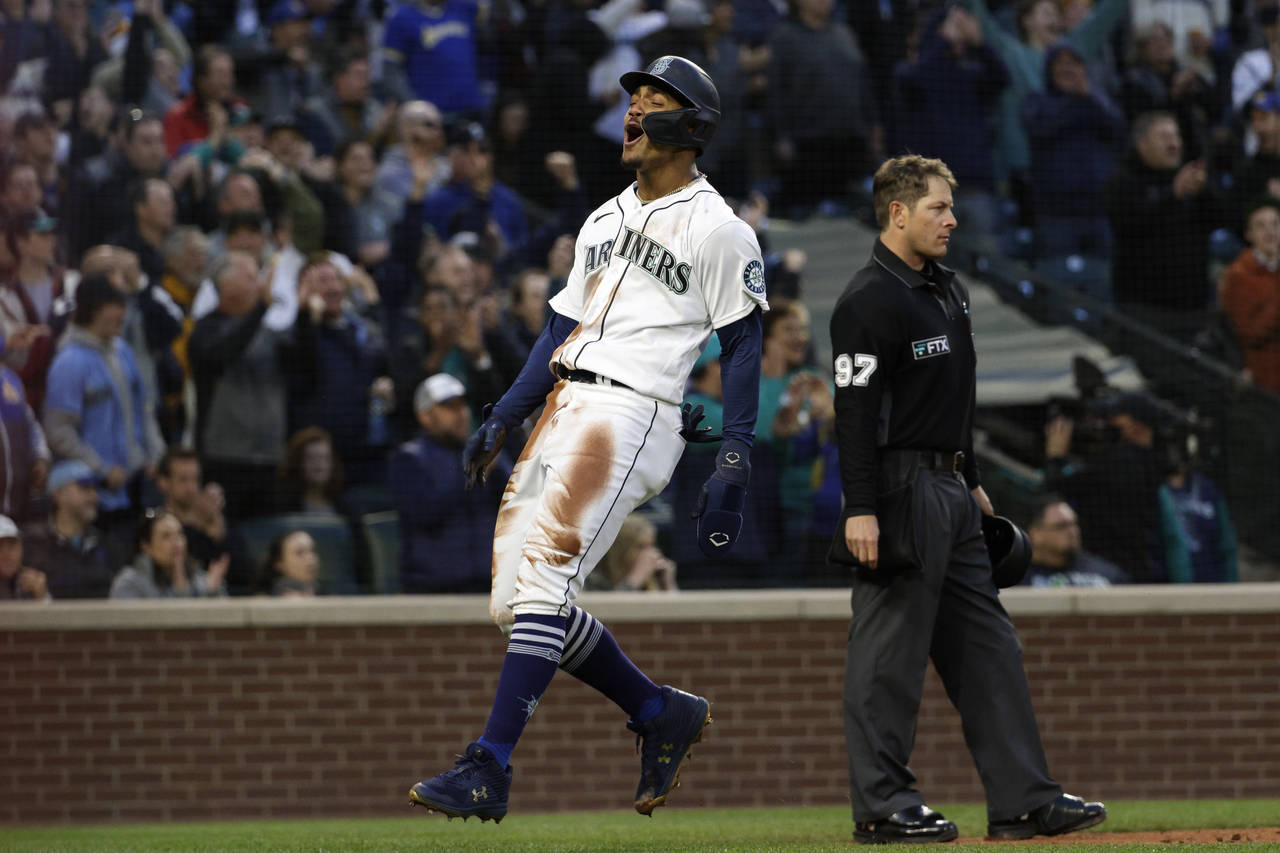 Seattle Mariners' Julio Rodriguez, left, reacts after scoring off a triple by Jarred Kelenic during...