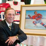 
              Former hockey star Guy Lafleur poses next to one of 10 paintings of moments from his career by artist Mario Beaudoin, Tuesday, May 18, 2004, in Montreal. Montreal Canadiens legend Guy Lafleur has died at age 70. (Paul Chiasson/The Canadian Press via AP)
            
