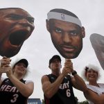
              FILE - Miami Heat fans Kristal Tamayo, left, Eddie Quintana, center, and his wife Nikki Quintana hold up huge cutout heads of Chris Bosh, LeBron James, and Dwyane Wade for a parade in Miami, June 25, 2012, in celebration of winning the NBA Finals basketball championship against the Oklahoma City Thunder. (AP Photo/Wilfredo Lee, File)
            