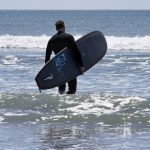 
              Dan Fischer, of Newport, R.I., walks into the ocean with his surfboard at Easton's Beach, in Newport, Wednesday, May 18, 2022. Fischer, 42, created the One Last Wave Project in January 2022 to use the healing power of the ocean to help families coping with a loss, as it helped him following the death of his father. Fischer places the names onto his surfboards, then takes the surfboards out into the ocean as a way to memorialize the lost loved ones in a place that was meaningful to them. (AP Photo/Steven Senne)
            