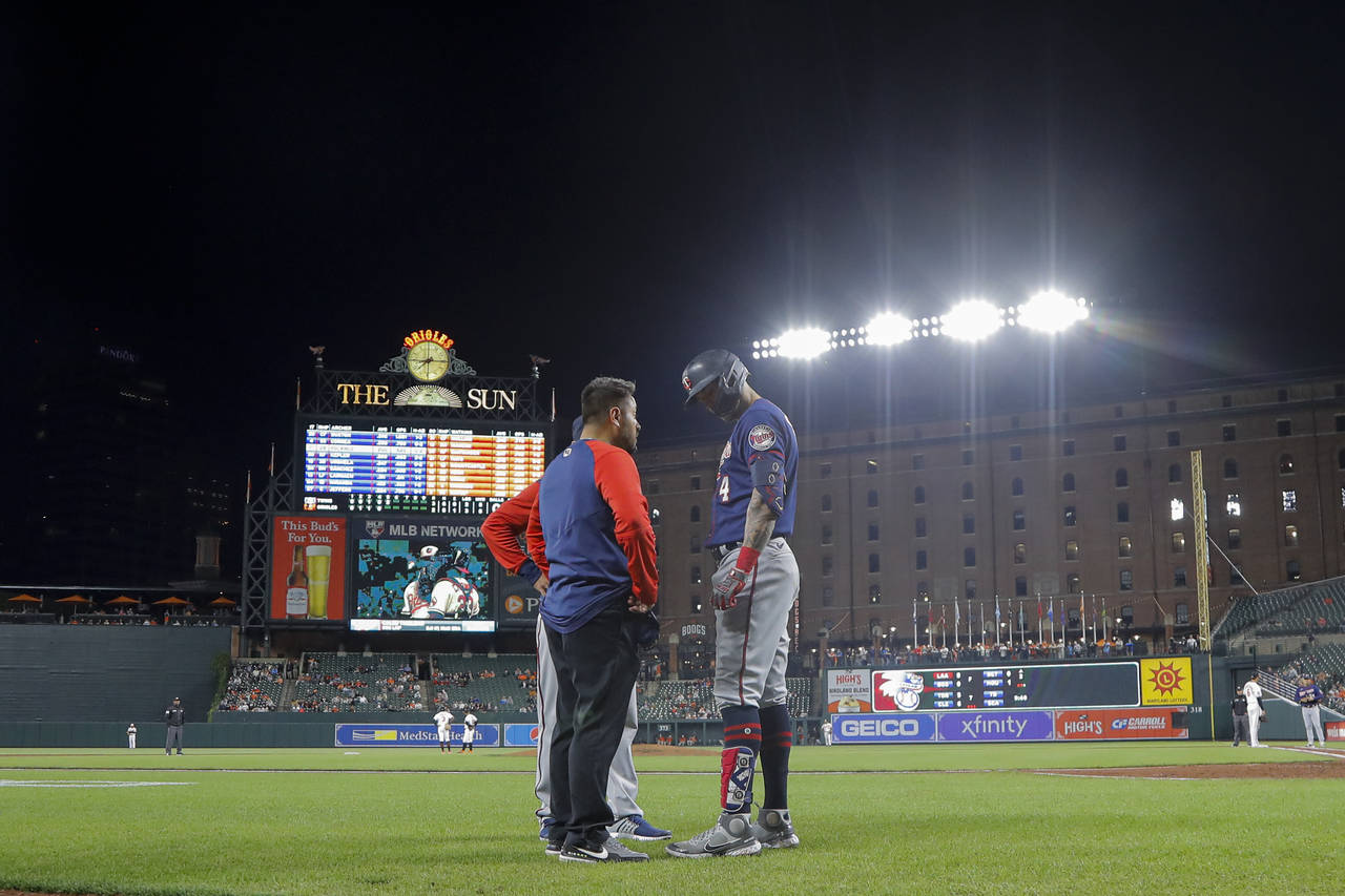A trainer talks to Minnesota Twins' Carlos Correa, right, after he was hit by a pitch from Baltimor...