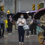 
              Commuters wearing face masks wait to cross an intersection on a rainy morning in Beijing, Friday, May 6, 2022. (AP Photo/Mark Schiefelbein)
            
