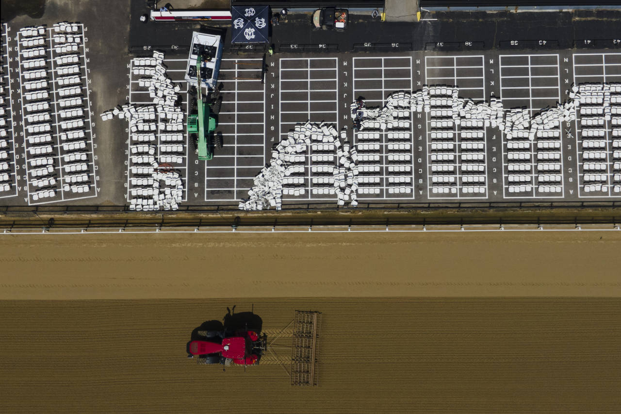 A tractors grooms the final straightaway at Pimlico Race Course near workers setting up seats ahead...