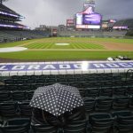 
              Fans huddle under a polka-dotted umbrella during a delay as light rain falls before the Colorado Rockies' baseball game against the Washington Nationals on Wednesday, May 4, 2022, in Denver. (AP Photo/David Zalubowski)
            