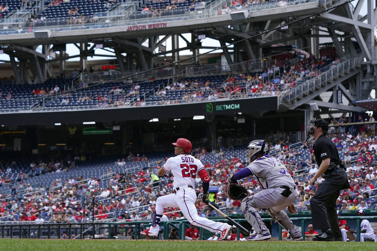 Washington Nationals' Juan Soto, left, hits a two-run home run in front of Colorado Rockies catcher...