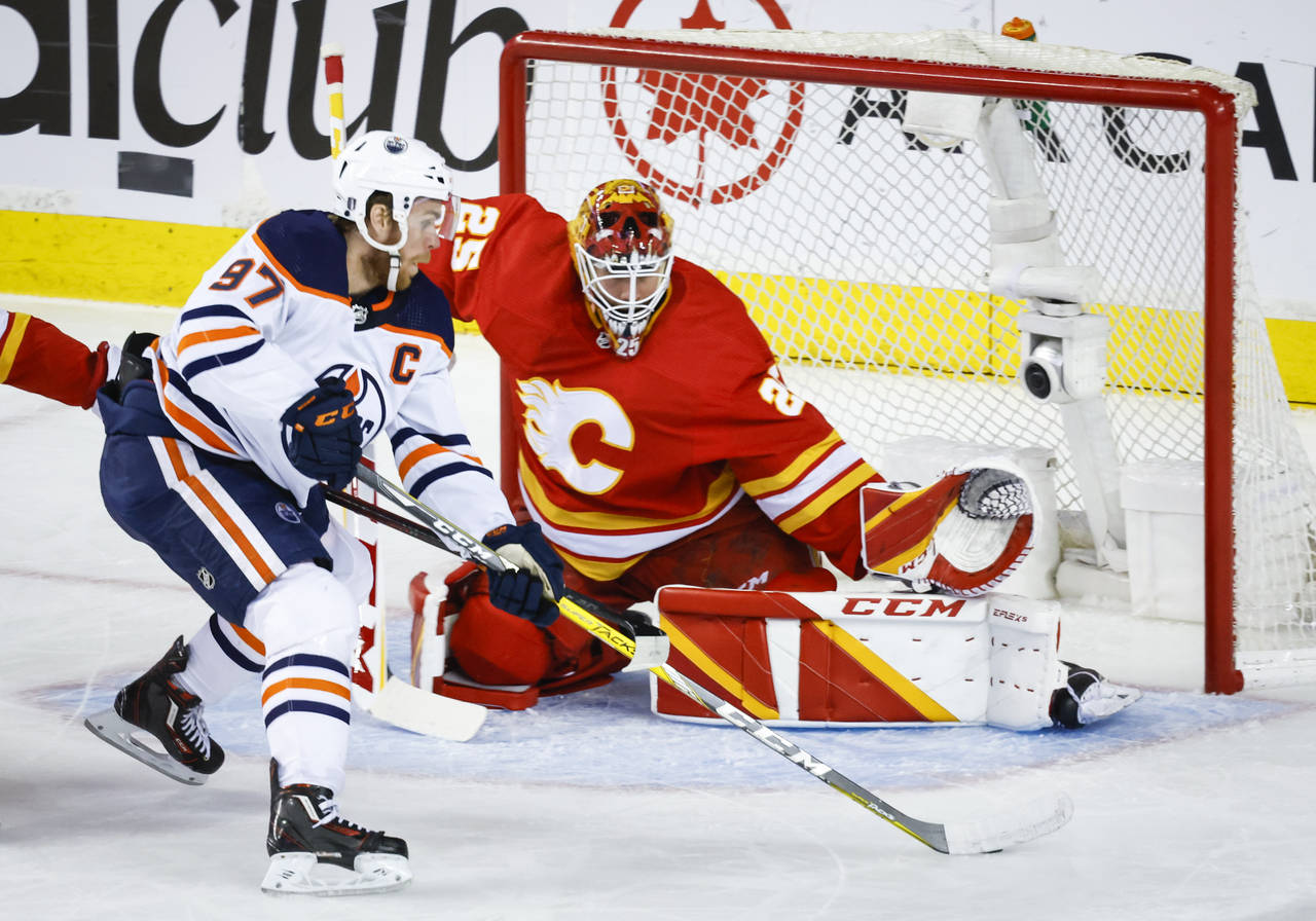 Edmonton Oilers center Connor McDavid, left, tries to get the puck past Calgary Flames goalie Jacob...