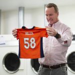 
              During filming for the Denver Broncos' 2021 schedule release video, former quarterback and current "intern" Peyton Peyton Manning washes a Von Miller jersey at UCHealth Training Center on Tuesday, May 10, 2021 in Englewood, Colo. Schedule release day has become a competition across the NFL between the social media departments of teams to see whose video creates the biggest impression. (Ben Swanson/Denver Broncos via AP)
            