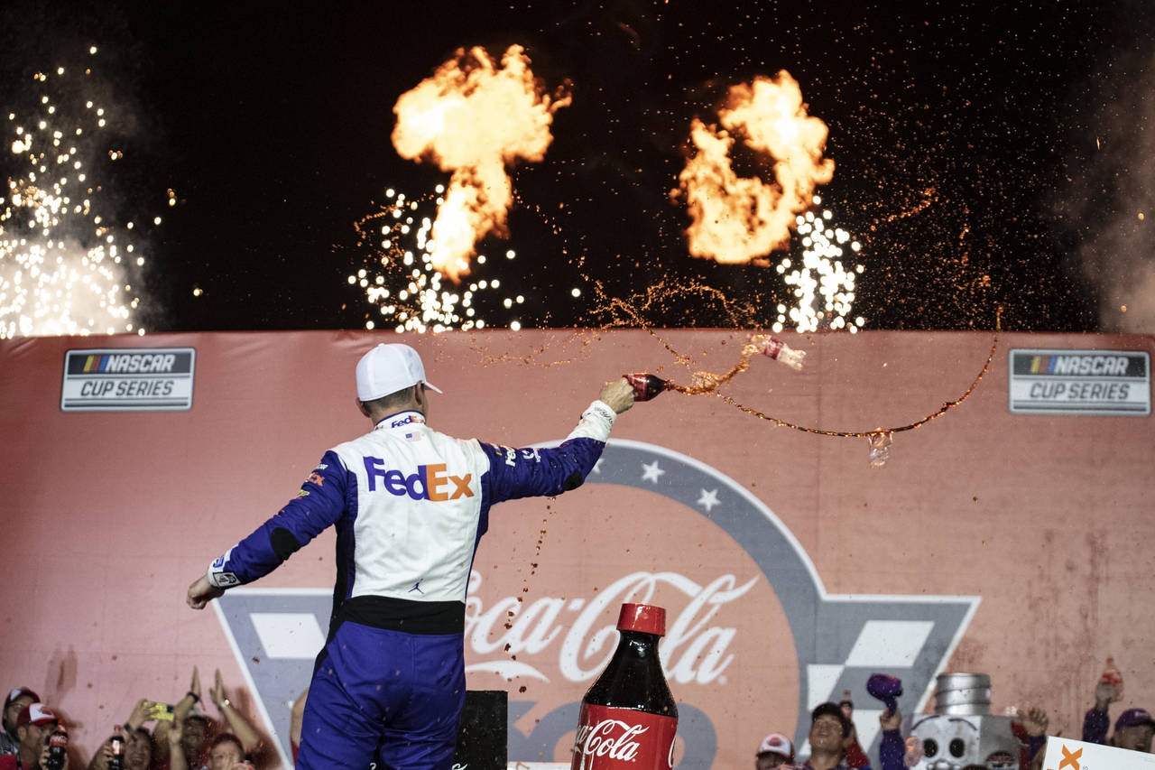 Denny Hamlin celebrates in Victory Lane after winning a NASCAR Cup Series auto race at Charlotte Mo...