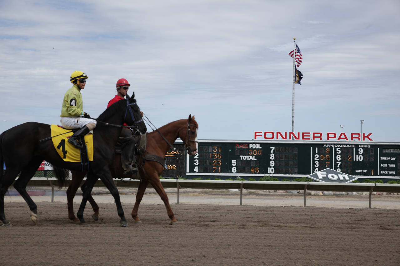 A jockey and handler ride their horses down the track between races at Fonner Park in Grand Island,...