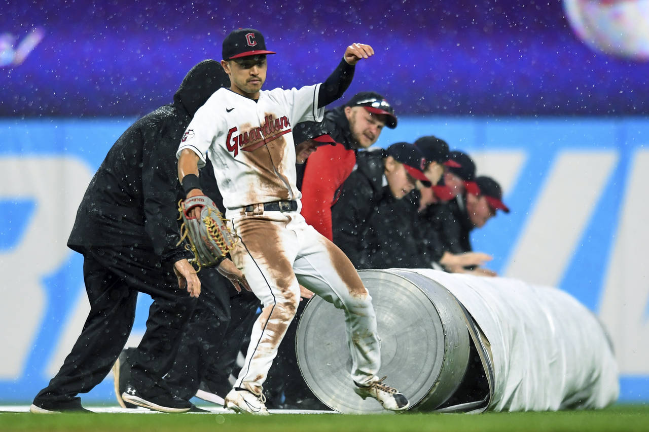 Cleveland Guardians' Steven Kwan avoids the grounds crew rolling out a tarp during a rain delay in ...