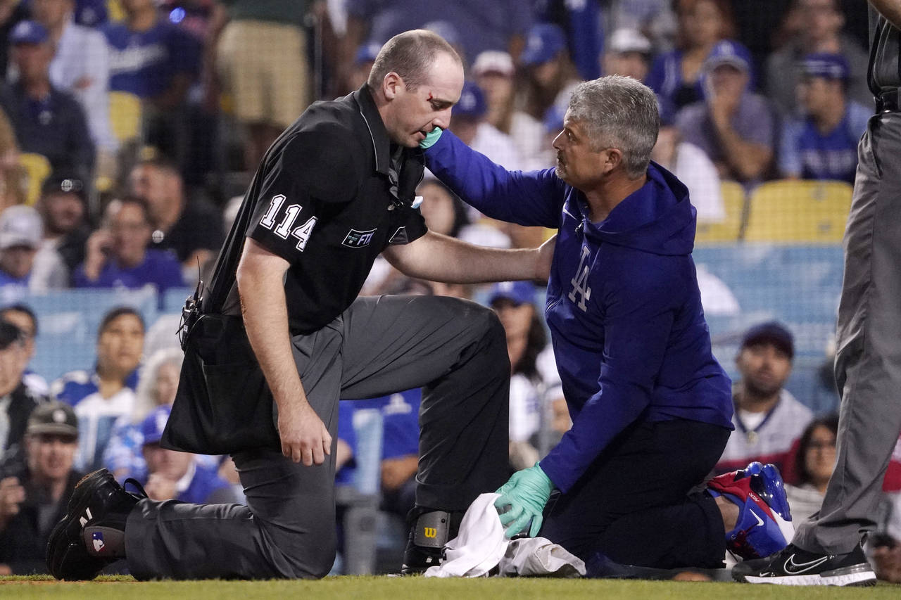 Home plate umpire Nate Tomlinson, left, is checked on by a Los Angeles Dodgers trainer after he was...