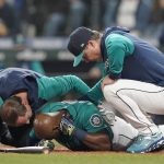 Seattle Mariners' Justin Upton, center, points to where he was hit by a pitch during the fifth inning of a baseball game against the Los Angeles Angels as he is examined by a trainer, left, and manager Scott Servais, right, Friday, June 17, 2022, in Seattle. Upton left the game after the injury. (AP Photo/Ted S. Warren)