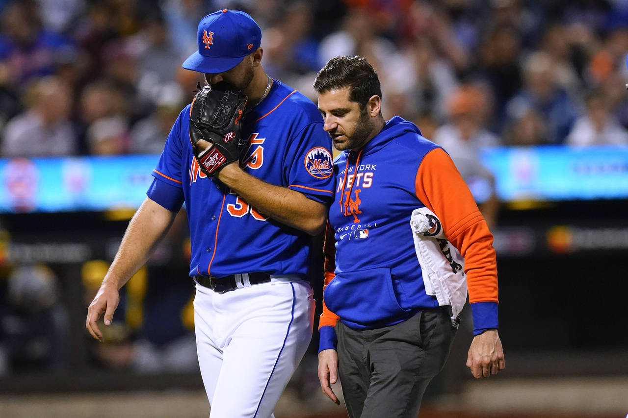 New York Mets starting pitcher Tylor Megill, left, talks to a trainer as he leaves during the fourt...