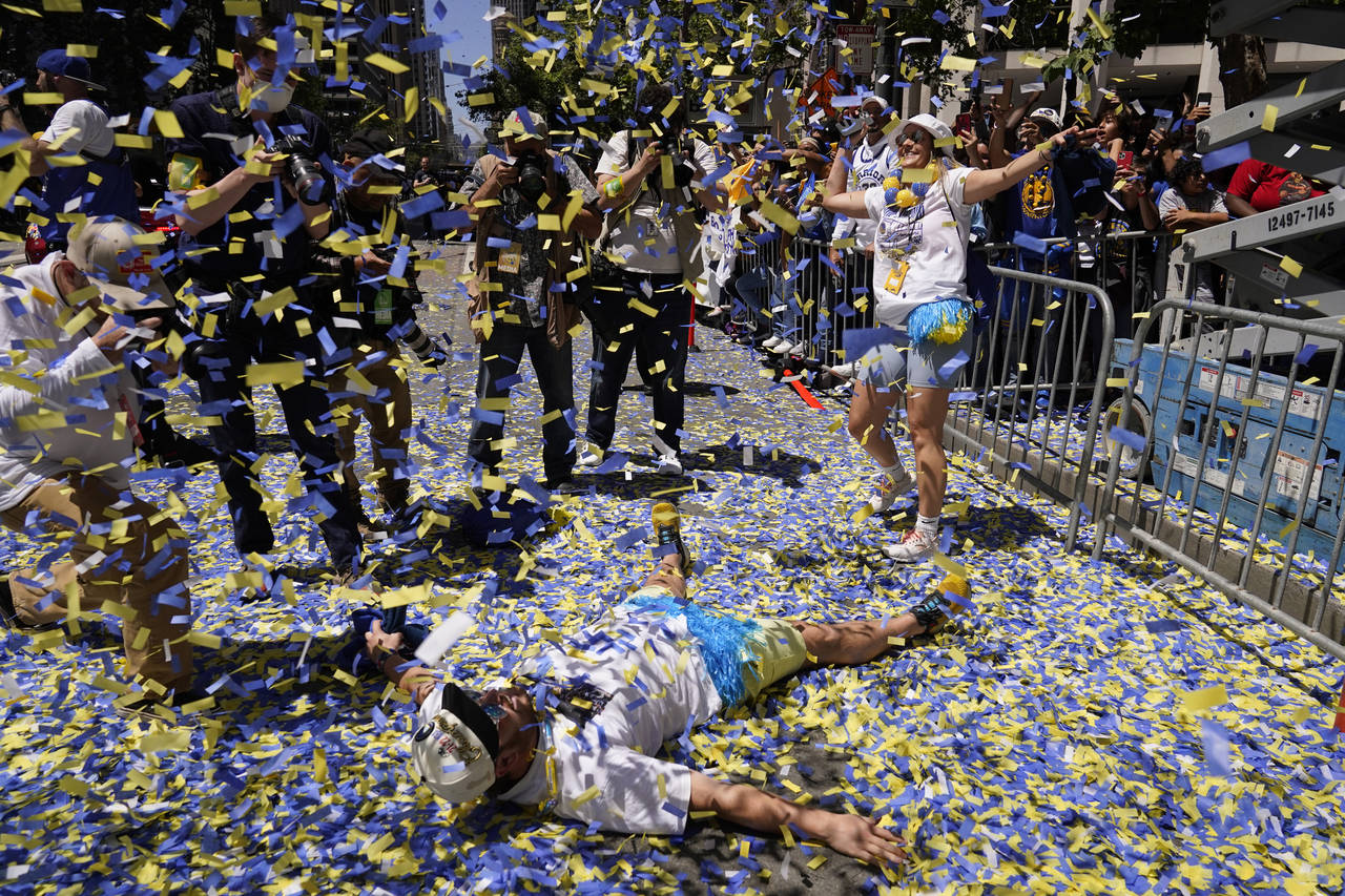 A man lays on Market Street as confetti rains during the Golden State Warriors NBA championship par...