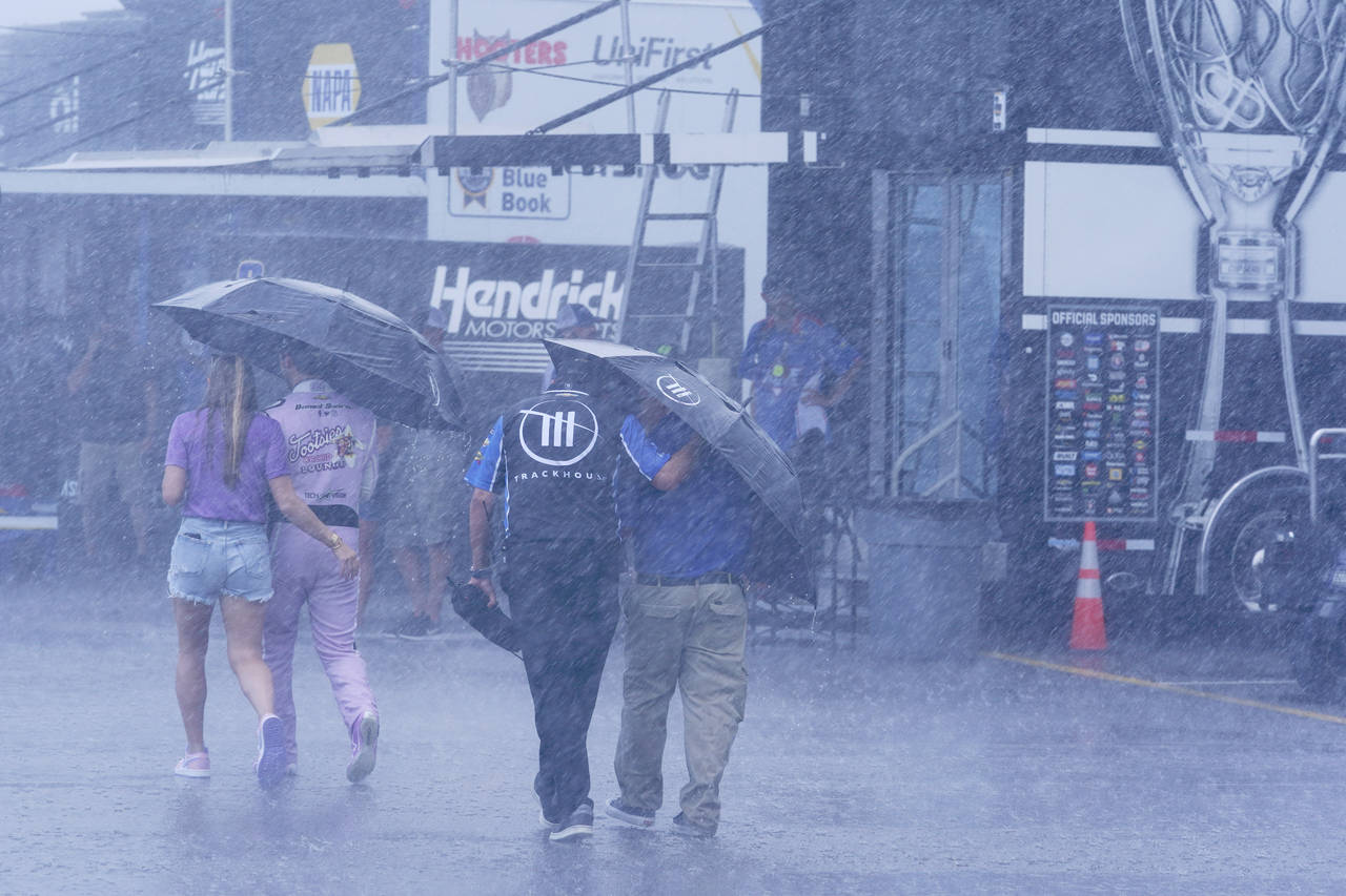 People walk through the track garage area during a rain shower before a NASCAR Xfinity Series auto ...