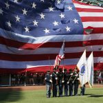 
              A giant United States flag drops in behind a military color guard during the national anthem before a baseball game between the Boston Red Sox and the Milwaukee Brewers, Saturday, July 30, 2022, in Boston. The Red Sox and the Home Base organization honored Black veterans during a pregame ceremony. (AP Photo/Michael Dwyer)
            