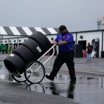 
              A crew member crosses a puddle with a cart of tires after a rain storm cancelled practice and qualifying for Saturday's NASCAR Truck Series auto race at Pocono Raceway, Friday, July 22, 2022, in Long Pond, Pa. (AP Photo/Matt Slocum)
            