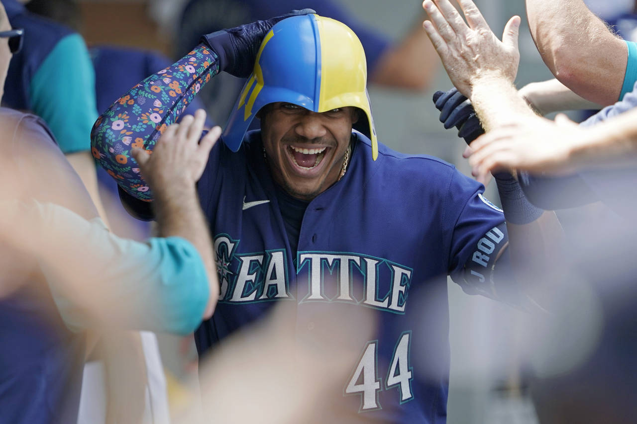 Seattle Mariners' Julio Rodriguez wears a helmet as he is greeted in the dugout after his three-run...
