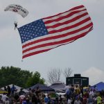 
              A parachuter holds a United States flag as he descends before a NASCAR Cup Series auto race Sunday, July 3, 2022, at Road America in Elkhart Lake, Wis. (AP Photo/Morry Gash)
            
