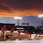 
              Grounds crew workers run with the tarp as the sun sets after a rain delay during the third inning of a baseball game between the Cleveland Guardians and the Boston Red Sox at Fenway Park, Monday, July 25, 2022, in Boston. (AP Photo/Charles Krupa)
            