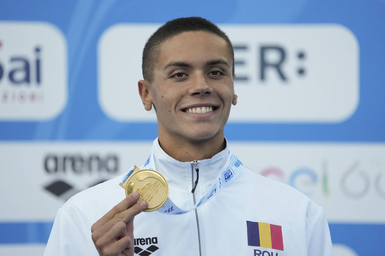 First placed Romania's David Popovici celebrates on the podium of the men's 100m freestyle final at...