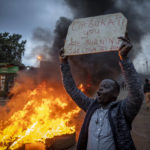 
              A supporter of presidential candidate Raila Odinga holds a placard referring to electoral commission chairman Wafula Chebukati, while shouting "No Raila, No Peace", next to a roadblock of burning tires in the Kibera neighborhood of Nairobi, Kenya Monday, Aug. 15, 2022. After last-minute chaos that could foreshadow a court challenge, Kenya's electoral commission chairman has declared Deputy President William Ruto the winner of the close presidential election over five-time contender Raila Odinga. (AP Photo/Ben Curtis)
            
