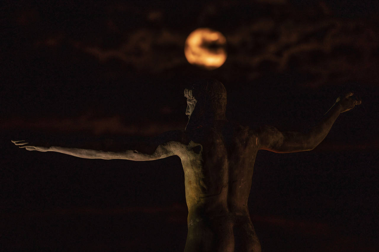 The Sturgeon moon rises behind a replica of an ancient bronze statue of Zeus or Poseidon, in Corint...