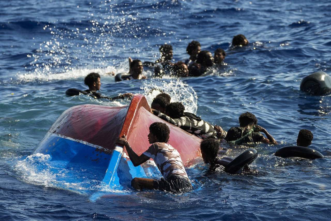 Migrants swim next to their overturned wooden boat during a rescue operation by Spanish NGO Open Ar...