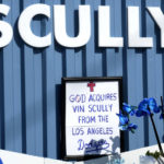 
              A framed not, "God Acquires Vin Scully From the Los Angeles Dodgers," is part of a growing makeshift memorial to Scully in front of the Welcome to Dodger Stadium sign along Vin Scully Avenue in Los Angeles on Wednesday, Aug. 3, 2022. Scully, whose 67-year career calling games in Brooklyn and Los Angeles made him the longest-tenured broadcaster with a single team in sports history, died Tuesday night at age 94. (Keith Birmingham/The Orange County Register via AP)
            