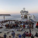 
              Migrants wait to board an Italian Coast Guard ship in the Sicilian Island of Lampedusa, Italy, Wednesday, Aug. 3, 2022. The migrants reception center on the island, which is also a summertime tourist destination, reached more than 1,500 people in a space designed, by his count, for 357. (AP Photo/David Lohmueller)
            