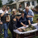 
              Lilia Panchenko is pulled away by her husband, Anatolii, right, as she says her final goodbye to their son, Oleh, along with his daughter, Ruslana, left, before his casket is covered during his burial service in Pokrovsk, Donetsk region, eastern Ukraine, Thursday, Aug. 4, 2022. Ukrainian soldier Oleh Panchenko, 48, was killed July 27 by Russian forces fighting in the Donetsk region. (AP Photo/David Goldman)
            