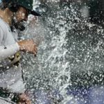 
              Oakland Athletics' Shea Langeliers is doused by Tony Kemp, not seen, as he gives a broadcast interview after the team's 5-1 win in a baseball game against the Texas Rangers in Arlington, Texas, Tuesday, Aug. 16, 2022. (AP Photo/Tony Gutierrez)
            