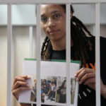 
              FILE - WNBA star and two-time Olympic gold medalist Brittney Griner holds images standing in a cage at a court room prior to a hearing, in Khimki just outside Moscow, Russia, Wednesday, July 27, 2022. (AP Photo/Alexander Zemlianichenko, Pool, File)
            