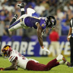 
              Baltimore Ravens running back Nate McCrary, top, flips over Washington Commanders safety Jeremy Reaves as he rushes the ball in the first half of a preseason NFL football game, Saturday, Aug. 27, 2022, in Baltimore. (AP Photo/Julio Cortez)
            