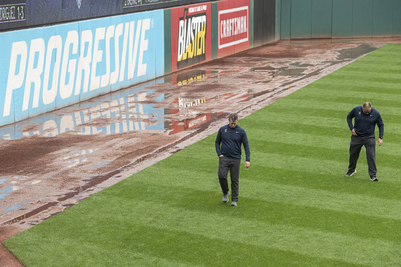 Members of the Cleveland Guardians ground crew inspect the left field turf at Progressive Field as ...